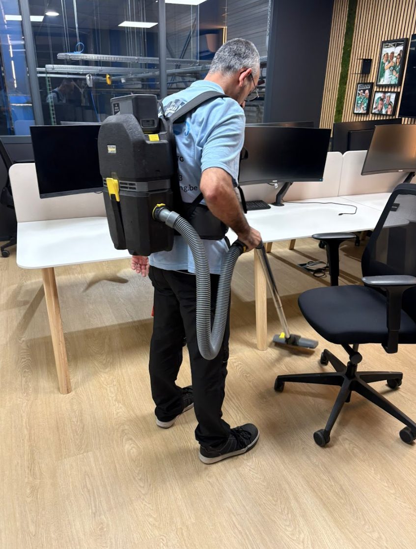 Medewerker van PM Cleaning met rugstofzuiger tussen de werkplekken